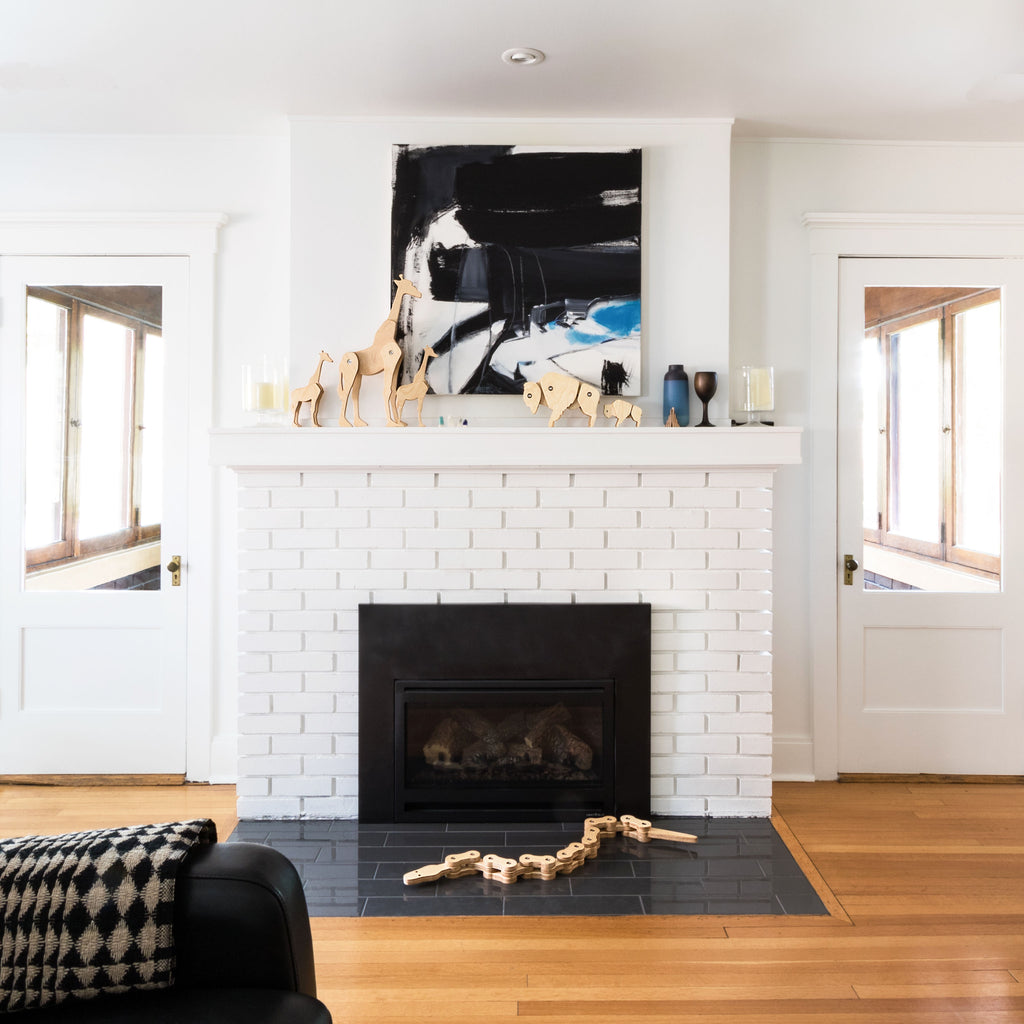 Modern white living room with Tectonic Giraffe family and Tectonic Bison Family on a white mantle in front of a modern painting, and the Tectonic Chain Snake on the grey tile hearth